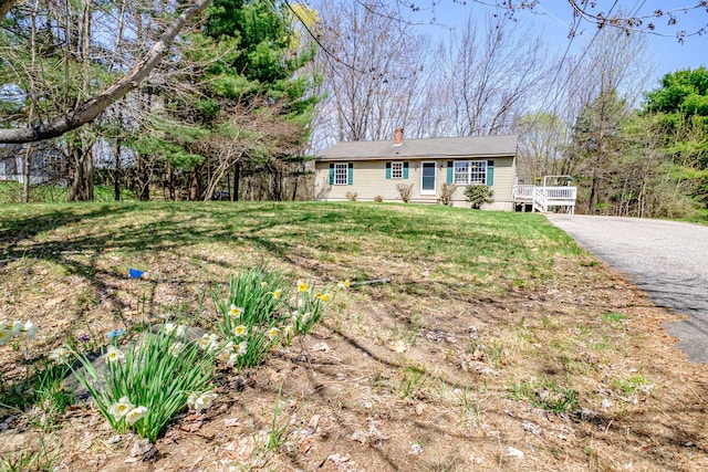 ranch-style house with a wooden deck, a front lawn, and a chimney