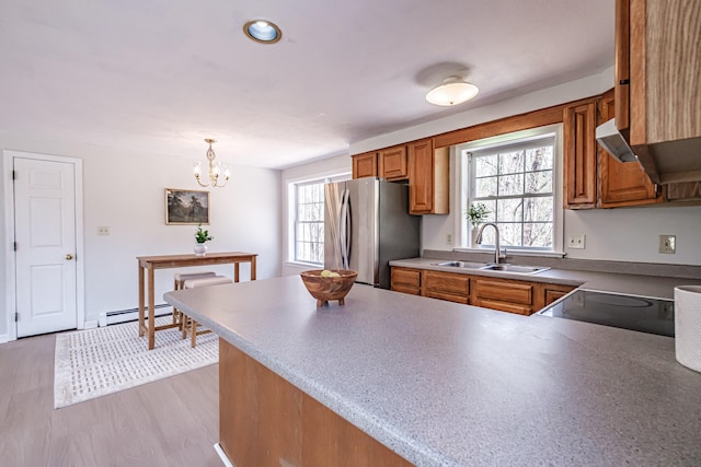 kitchen featuring brown cabinets, a sink, a baseboard radiator, freestanding refrigerator, and a peninsula