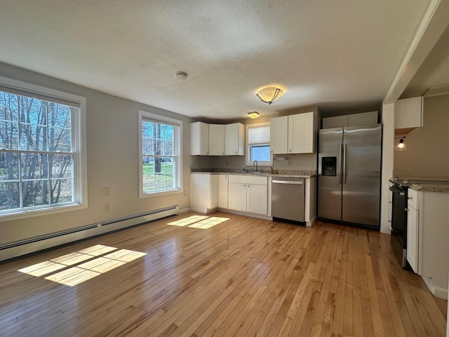 kitchen featuring a sink, a textured ceiling, light wood-style flooring, stainless steel appliances, and a baseboard radiator