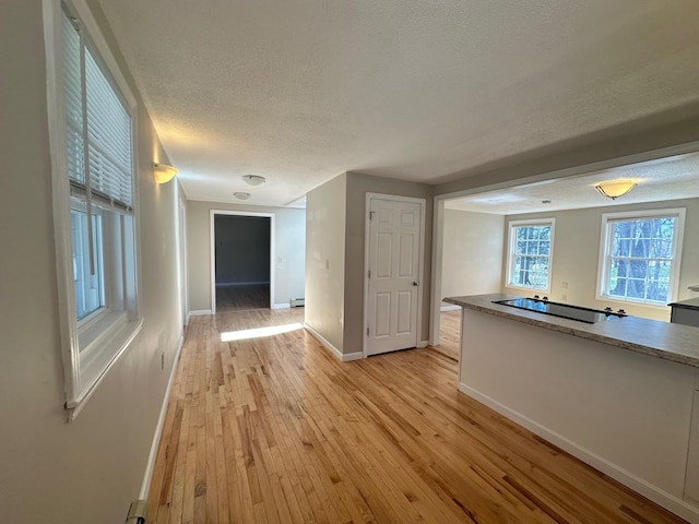 hallway with baseboards, a textured ceiling, light wood finished floors, and baseboard heating