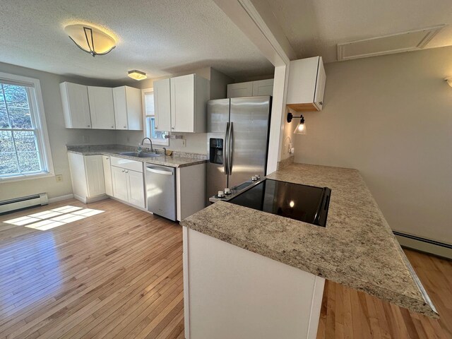 kitchen featuring baseboard heating, light wood-type flooring, white cabinetry, a sink, and stainless steel appliances