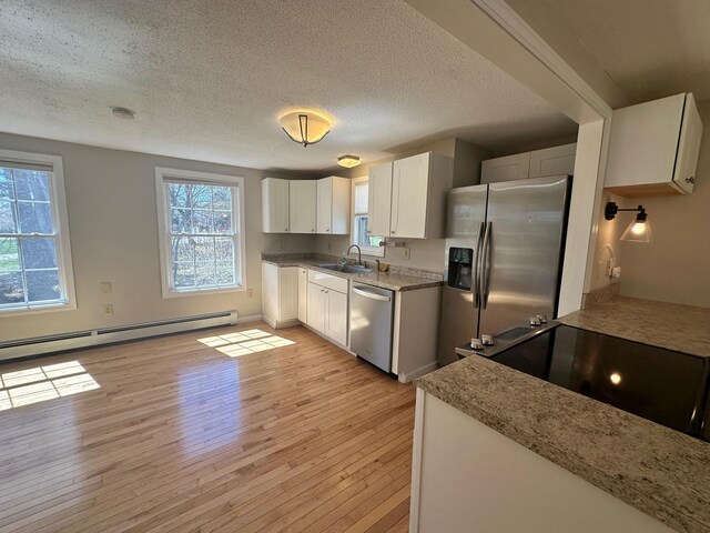 kitchen with light wood-style floors, baseboard heating, a textured ceiling, a sink, and stainless steel appliances