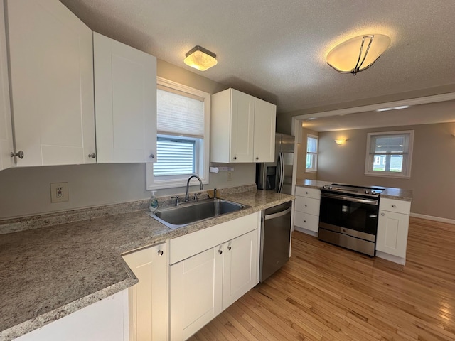 kitchen featuring appliances with stainless steel finishes, a sink, a textured ceiling, light wood-style flooring, and white cabinetry