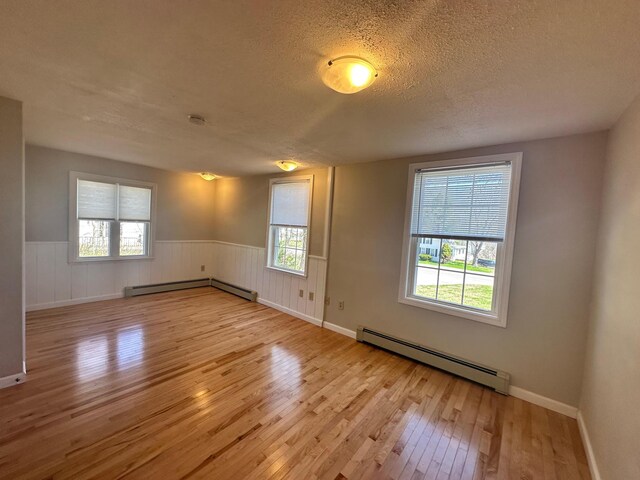 spare room with a textured ceiling, wainscoting, baseboard heating, and hardwood / wood-style floors