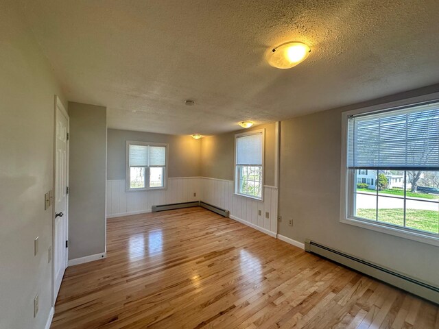 empty room featuring a textured ceiling, a baseboard radiator, a wealth of natural light, and hardwood / wood-style floors