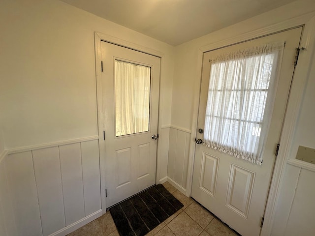 doorway to outside featuring a wainscoted wall, light tile patterned floors, and a decorative wall