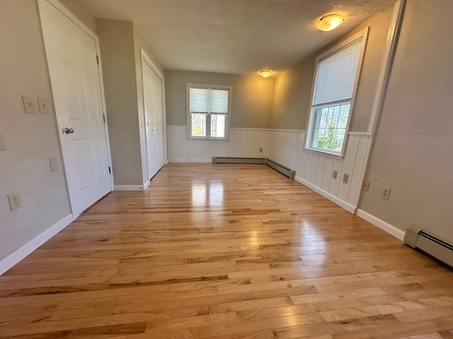 unfurnished room featuring a baseboard heating unit, plenty of natural light, a wainscoted wall, and light wood-style floors
