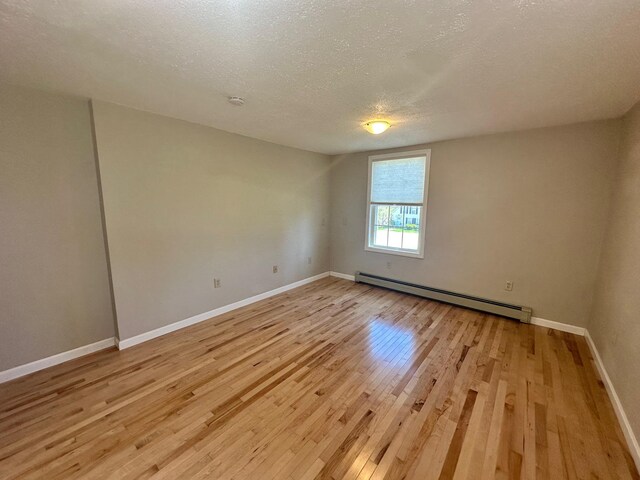 empty room featuring a textured ceiling, a baseboard heating unit, baseboards, and light wood-style floors