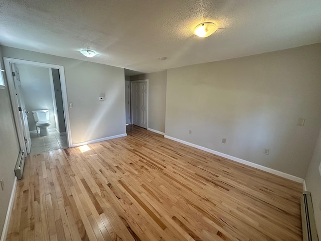empty room featuring baseboards, a baseboard radiator, light wood-type flooring, and a textured ceiling