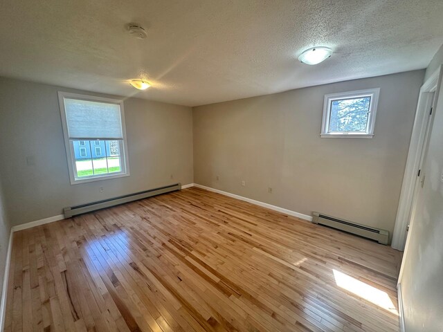 empty room with a textured ceiling, baseboards, baseboard heating, and light wood-style floors