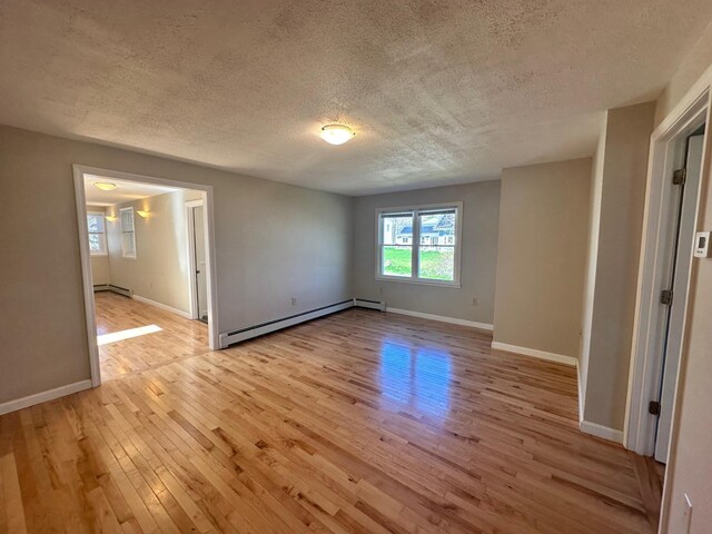 empty room featuring baseboards, a baseboard heating unit, light wood-type flooring, and a textured ceiling