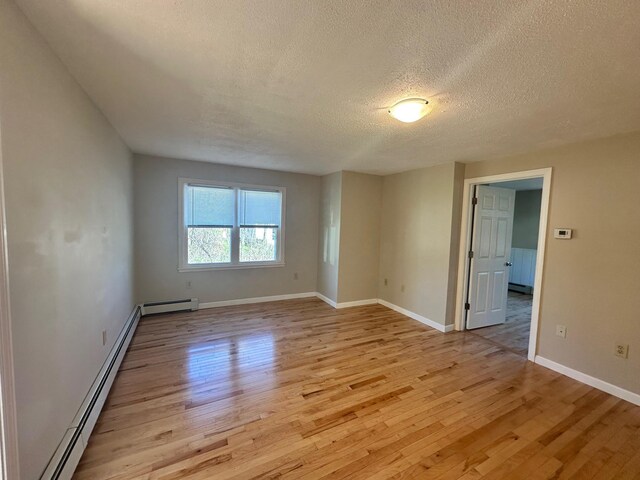 spare room with light wood-style floors, a baseboard radiator, a textured ceiling, and baseboards