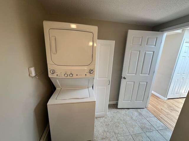 washroom with light tile patterned flooring, a textured ceiling, stacked washing maching and dryer, and baseboards