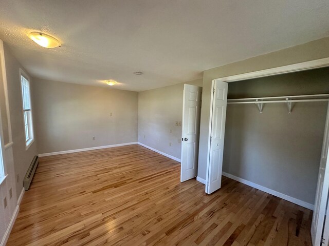 unfurnished bedroom featuring a closet, baseboards, a baseboard heating unit, and light wood finished floors