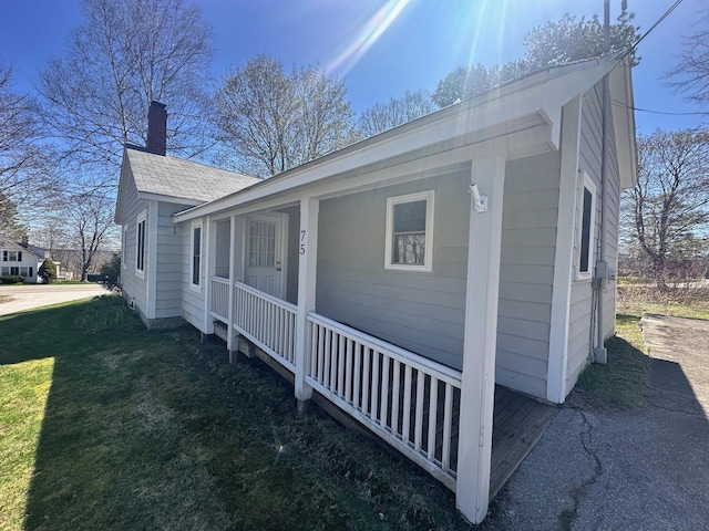 view of front of property featuring a porch, a chimney, a shingled roof, and a front lawn