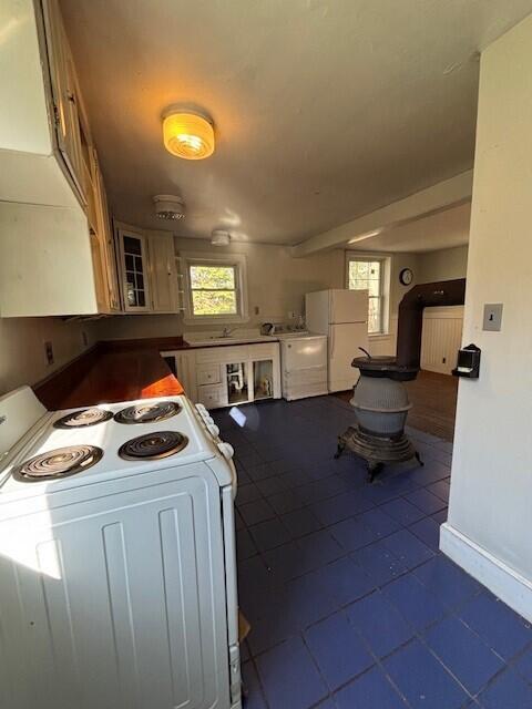 kitchen featuring dark tile patterned floors, baseboards, a wealth of natural light, and white appliances