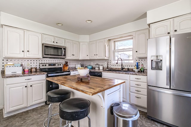 kitchen featuring appliances with stainless steel finishes, a sink, wooden counters, white cabinetry, and backsplash
