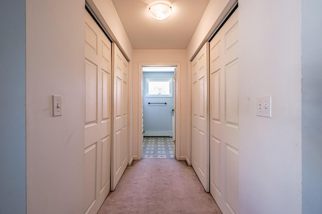 corridor with a baseboard heating unit and light carpet