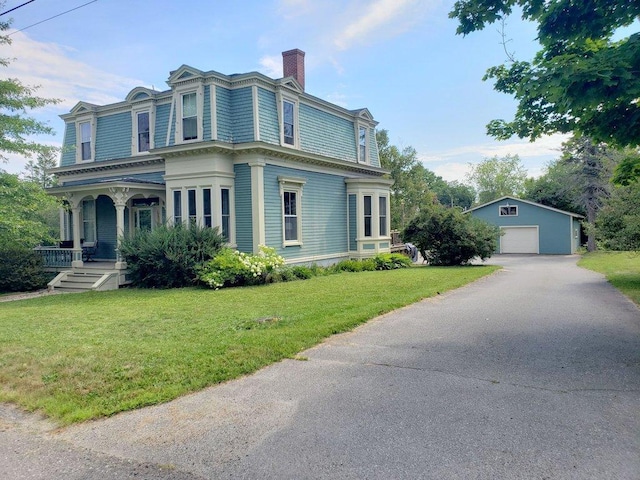 view of front of home featuring a front yard, a garage, an outbuilding, covered porch, and a chimney