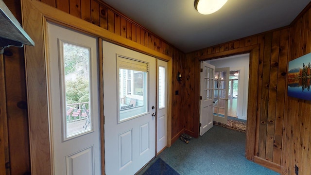 entryway featuring wooden walls and dark carpet