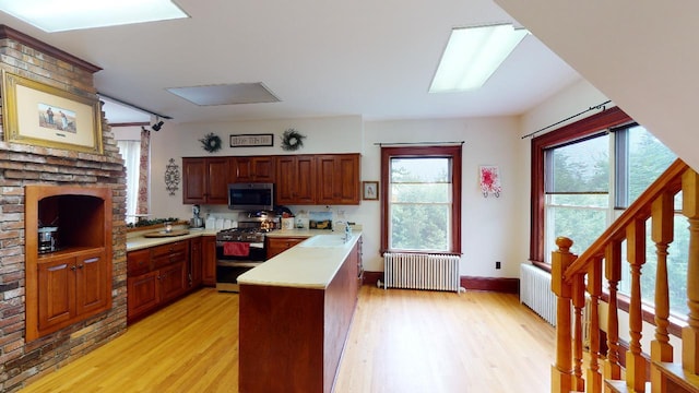 kitchen with stainless steel microwave, gas range oven, light wood-type flooring, radiator heating unit, and a peninsula