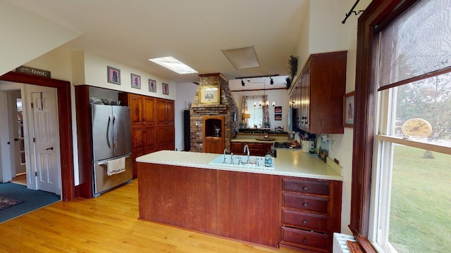 kitchen featuring light wood-style flooring, a sink, light countertops, freestanding refrigerator, and a peninsula
