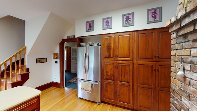 kitchen with light wood-style flooring, light countertops, freestanding refrigerator, baseboards, and brown cabinetry