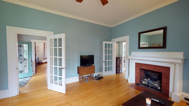 living room featuring wood finished floors, ceiling fan, french doors, a fireplace with flush hearth, and crown molding