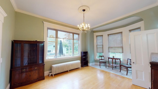 dining area with radiator heating unit, arched walkways, light wood-style floors, and crown molding