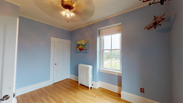 unfurnished room with radiator, crown molding, a ceiling fan, baseboards, and wood finished floors