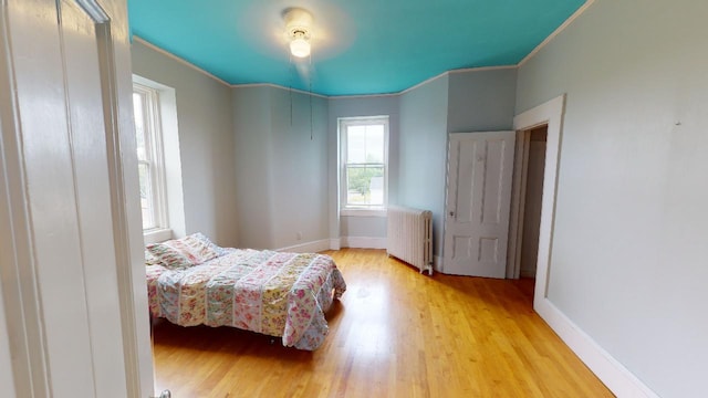bedroom with radiator heating unit, wood finished floors, crown molding, and baseboards