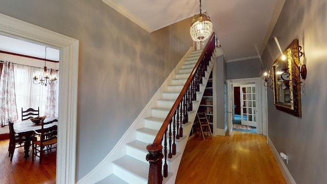 staircase with wood finished floors, a chandelier, ornamental molding, and baseboards