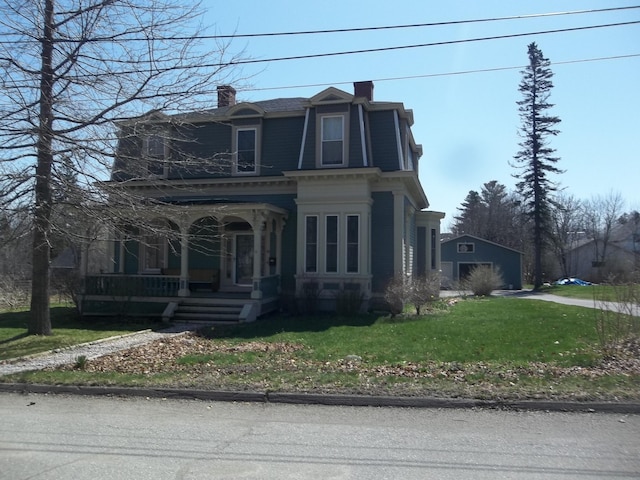 victorian home featuring a porch, a front yard, a detached garage, a chimney, and mansard roof