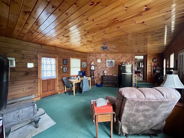 living area with a wood stove, wooden ceiling, a ceiling fan, wood walls, and carpet floors