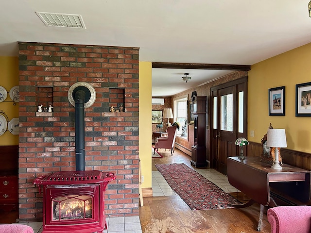 living area featuring light tile patterned floors, a wood stove, visible vents, a wainscoted wall, and a baseboard heating unit