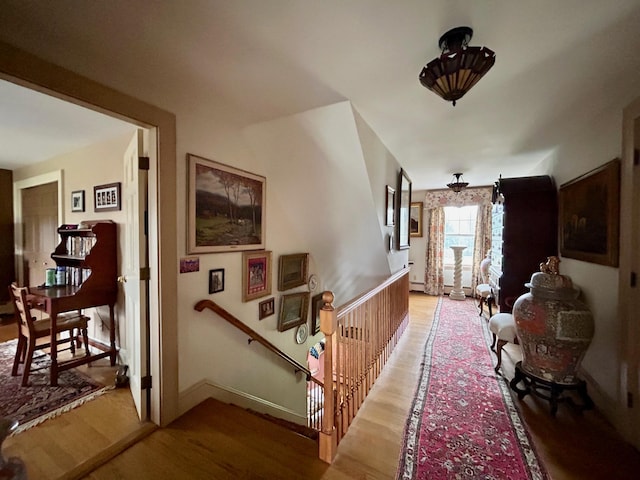 corridor with baseboards, an upstairs landing, and light wood-style flooring