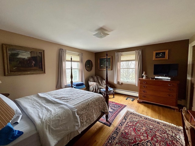 bedroom featuring baseboard heating, multiple windows, and light wood-style flooring