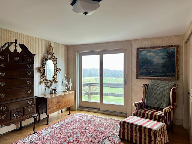 sitting room with wallpapered walls, wood finished floors, and a baseboard heating unit