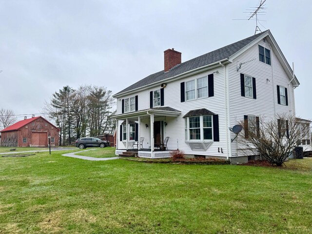 colonial home featuring covered porch, a chimney, and a front yard