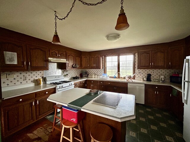 kitchen with under cabinet range hood, white appliances, a center island, backsplash, and light countertops