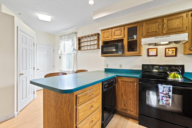 kitchen featuring under cabinet range hood, brown cabinetry, a peninsula, black appliances, and light wood-style floors