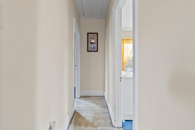 corridor featuring light carpet, attic access, and baseboards