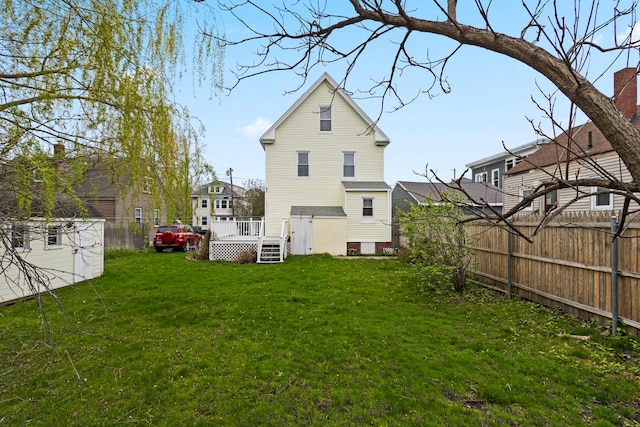 rear view of house featuring a wooden deck, fence, and a lawn