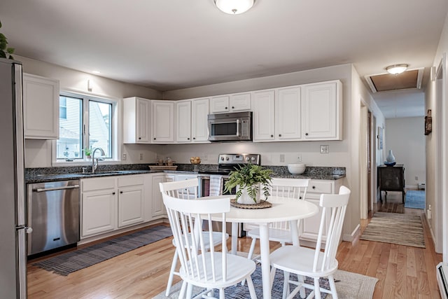 kitchen with a sink, appliances with stainless steel finishes, white cabinets, and light wood-style floors