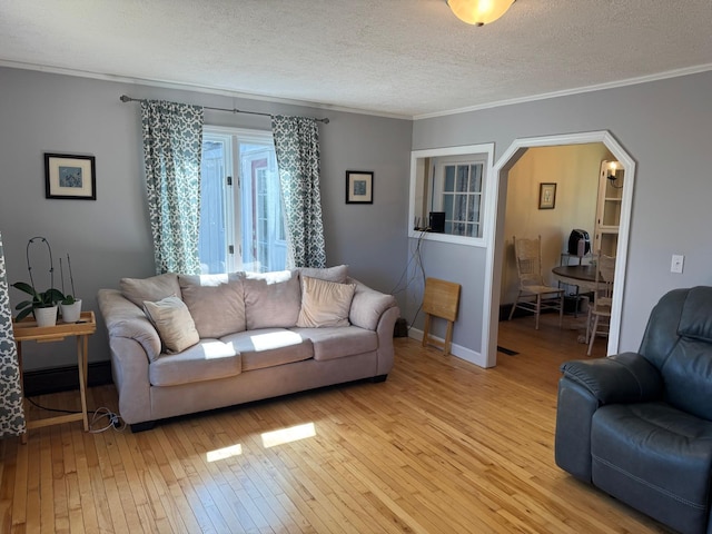 living area with arched walkways, light wood-type flooring, crown molding, baseboards, and a textured ceiling