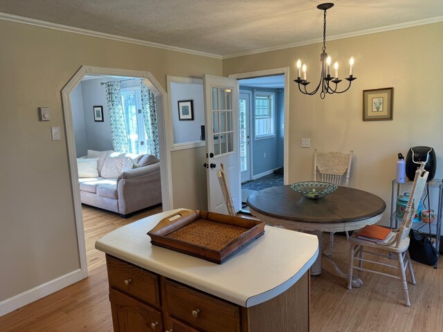 dining space featuring a chandelier, light wood-type flooring, baseboards, ornamental molding, and arched walkways
