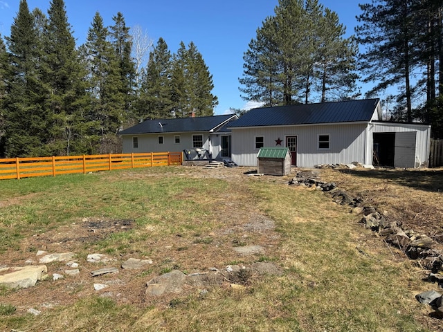 back of property with fence, an outdoor structure, a yard, and metal roof
