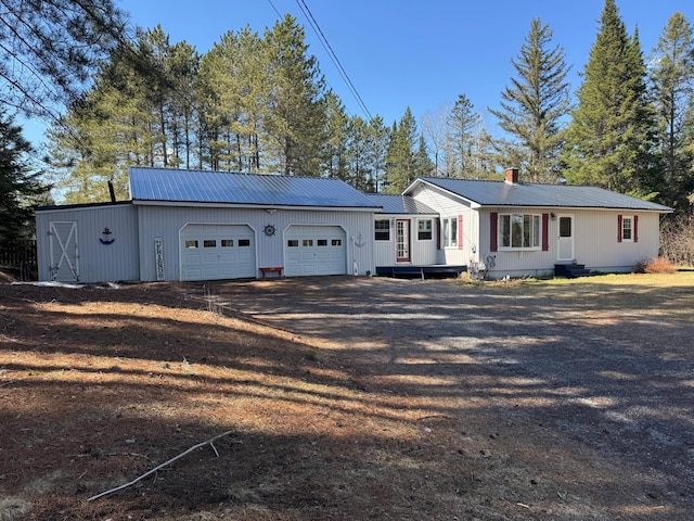 ranch-style home with a garage, dirt driveway, and metal roof