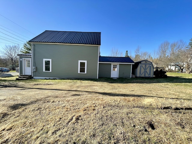rear view of house with an outdoor structure, entry steps, metal roof, a shed, and a yard