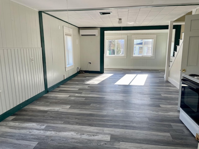 unfurnished living room with wood finished floors, stairs, a wall mounted AC, baseboards, and visible vents